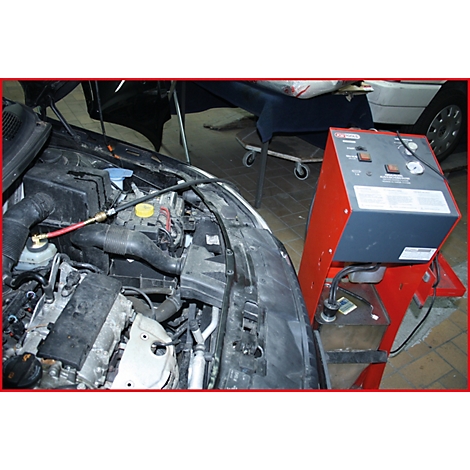 Ein offener Motorraum mit angeschlossenen Messgeräten und einer roten, grauen Apparatur. Im Hintergrund ein weiterer Wagen.